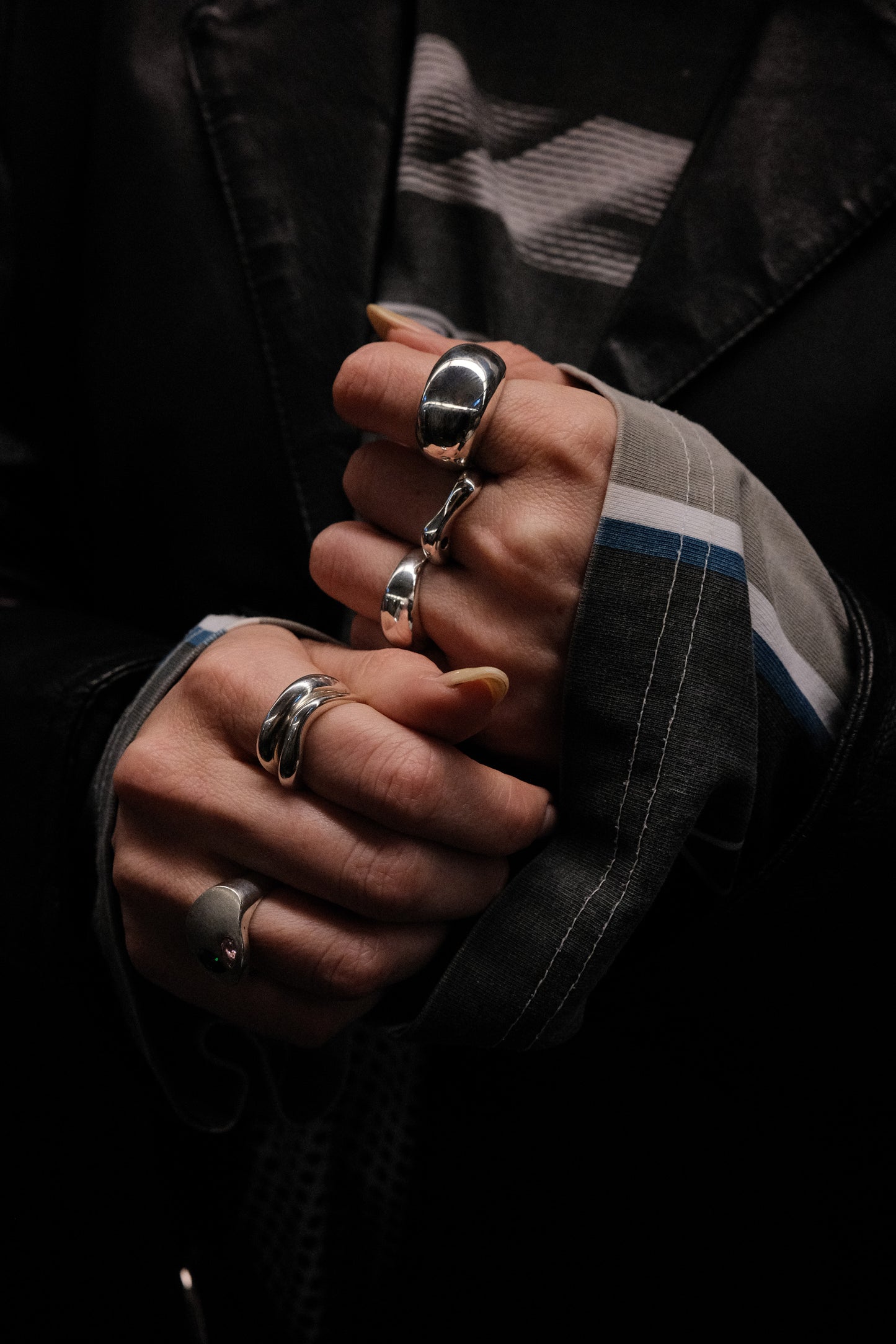 Close-up of hands with multiple rings on fingers against a dark underground background