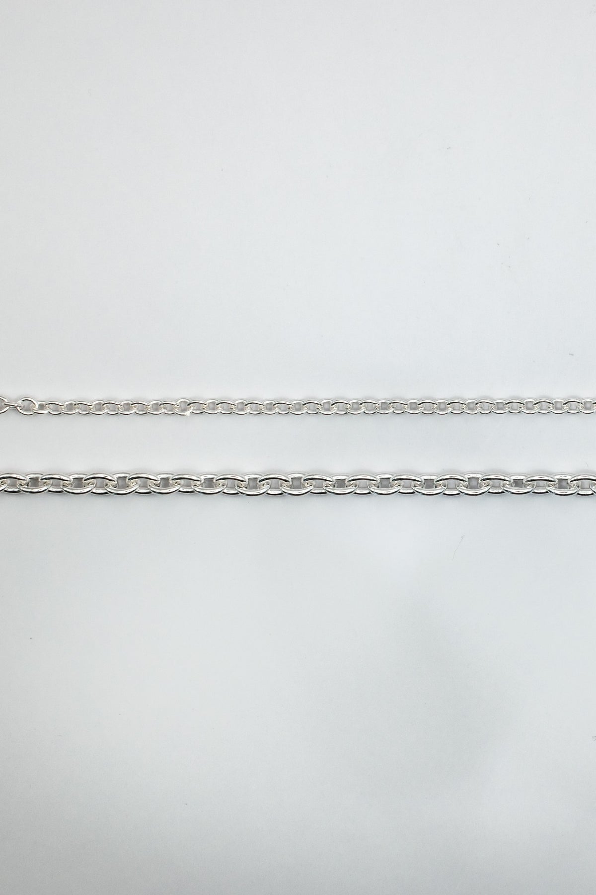 A close-up of a silver metal chain options laid horizontally on a plain light gray background.
