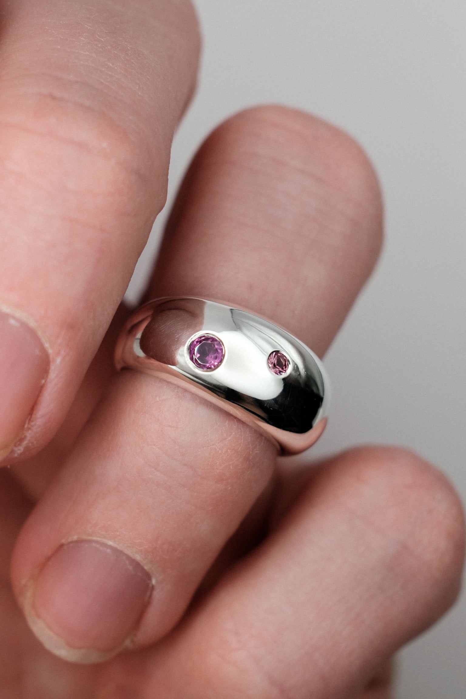 Silver ring with pink gemstones on a finger against a neutral background