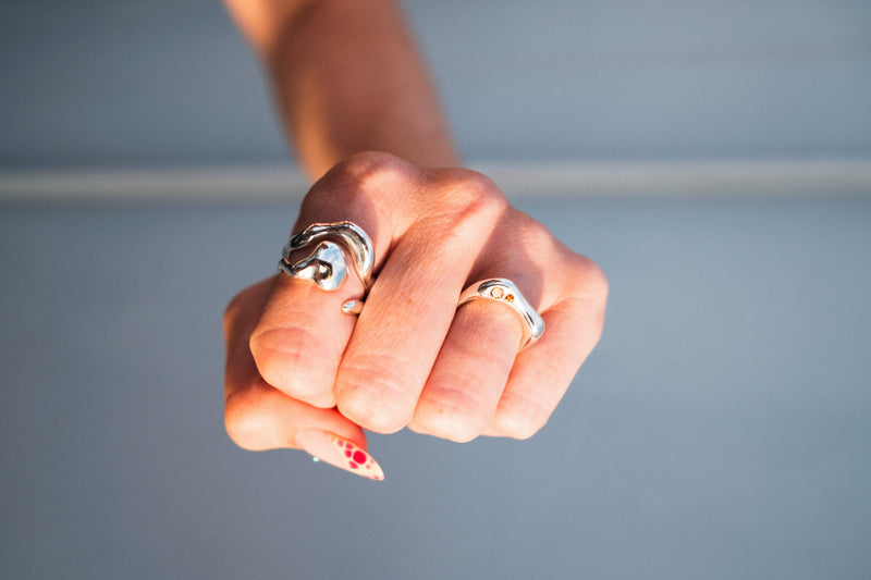 Close-up of a hand wearing two silver rings with a blurred gray background