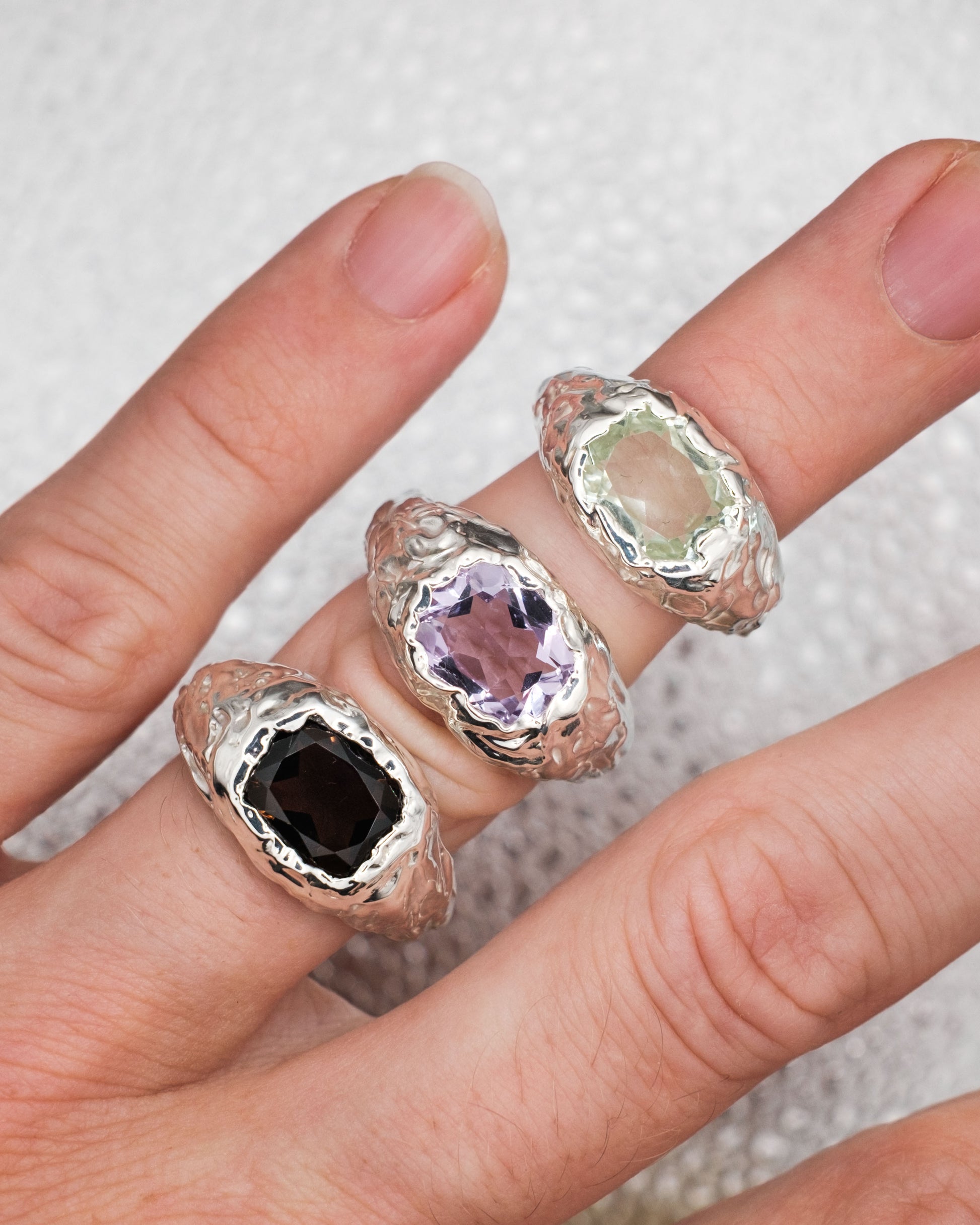 Three silver rings with color gemstones on a hand against a neutral background