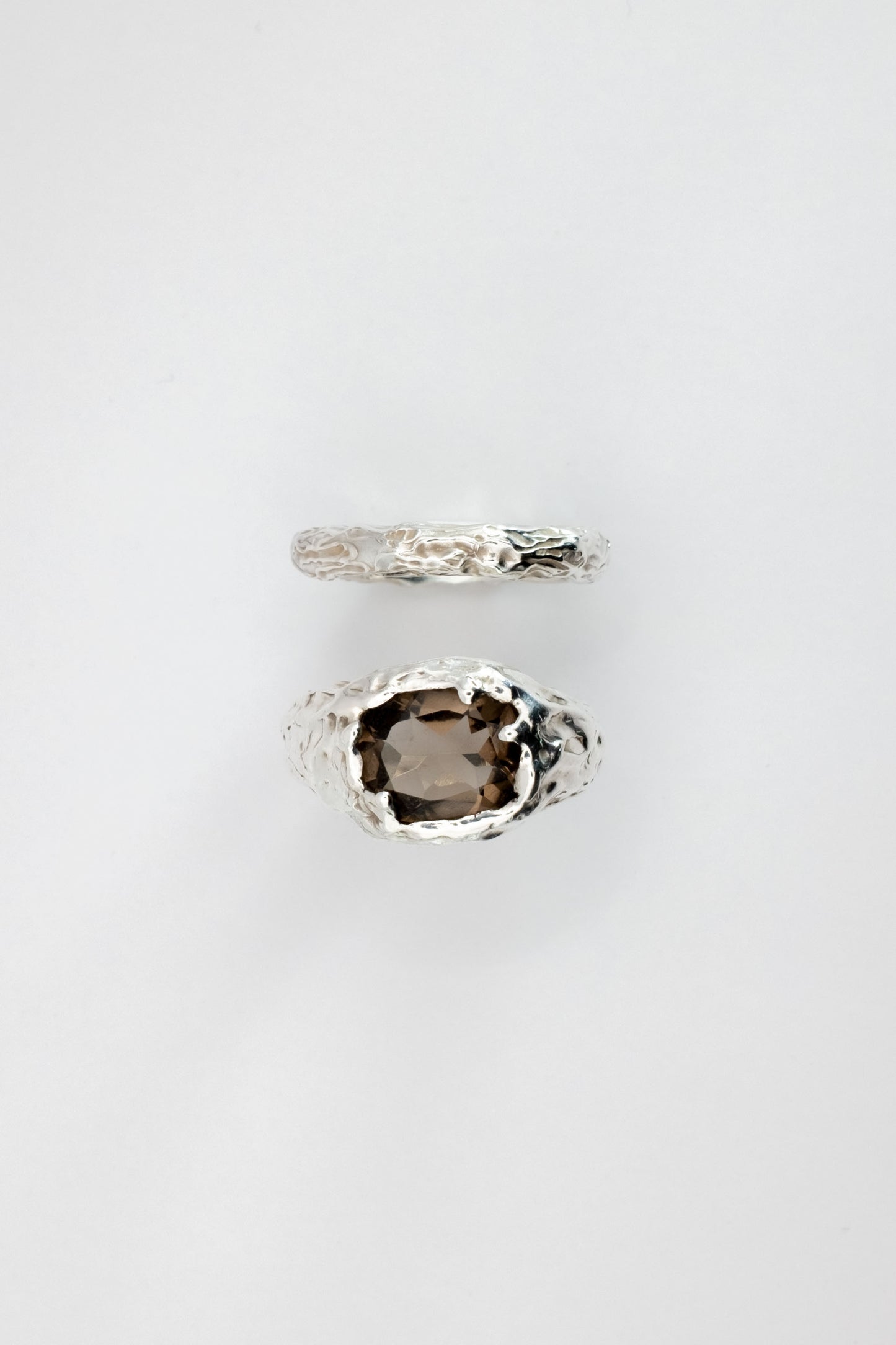 Two liquid surface rings with gemstones on a light gray background