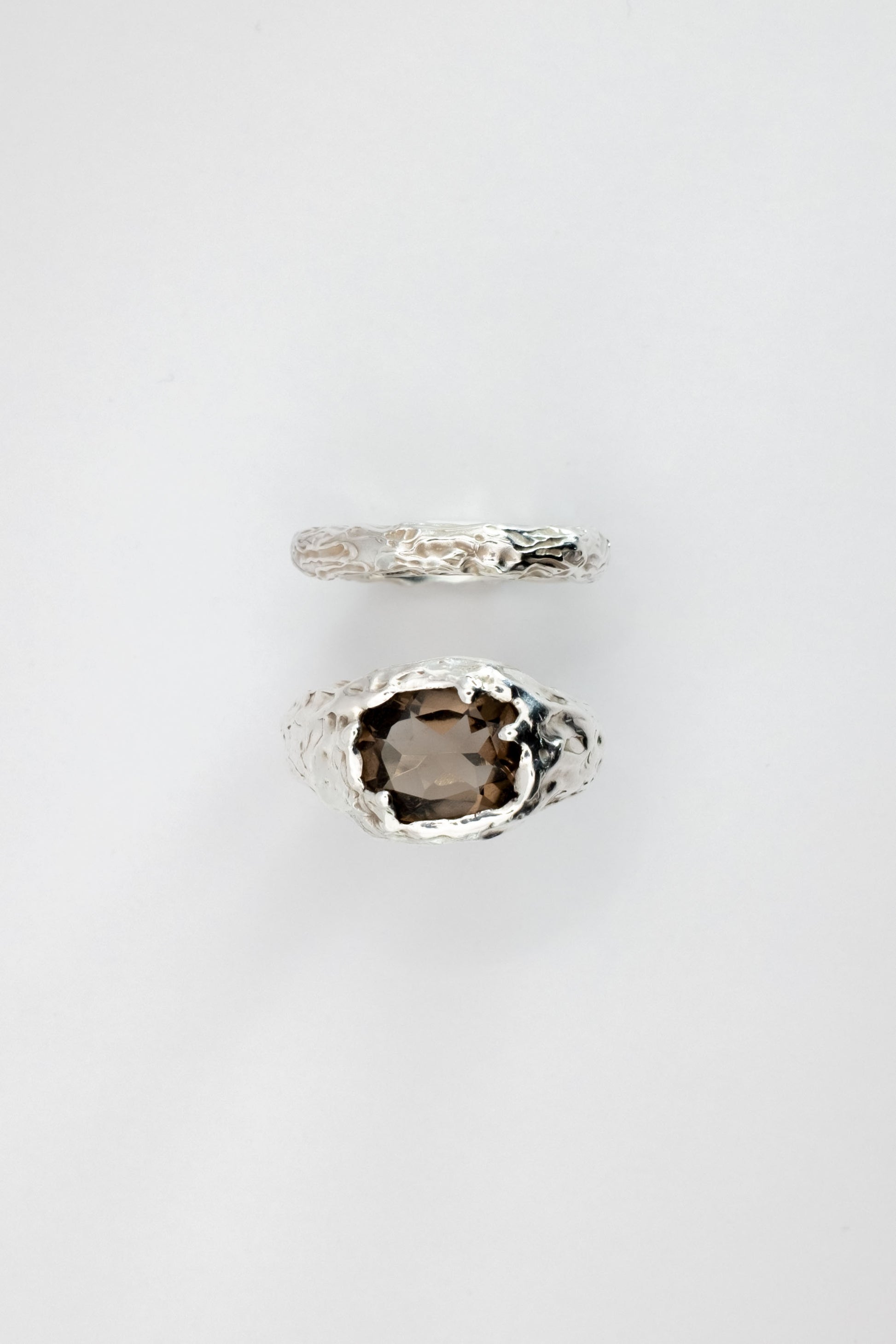 Two liquid surface rings with gemstones on a light gray background