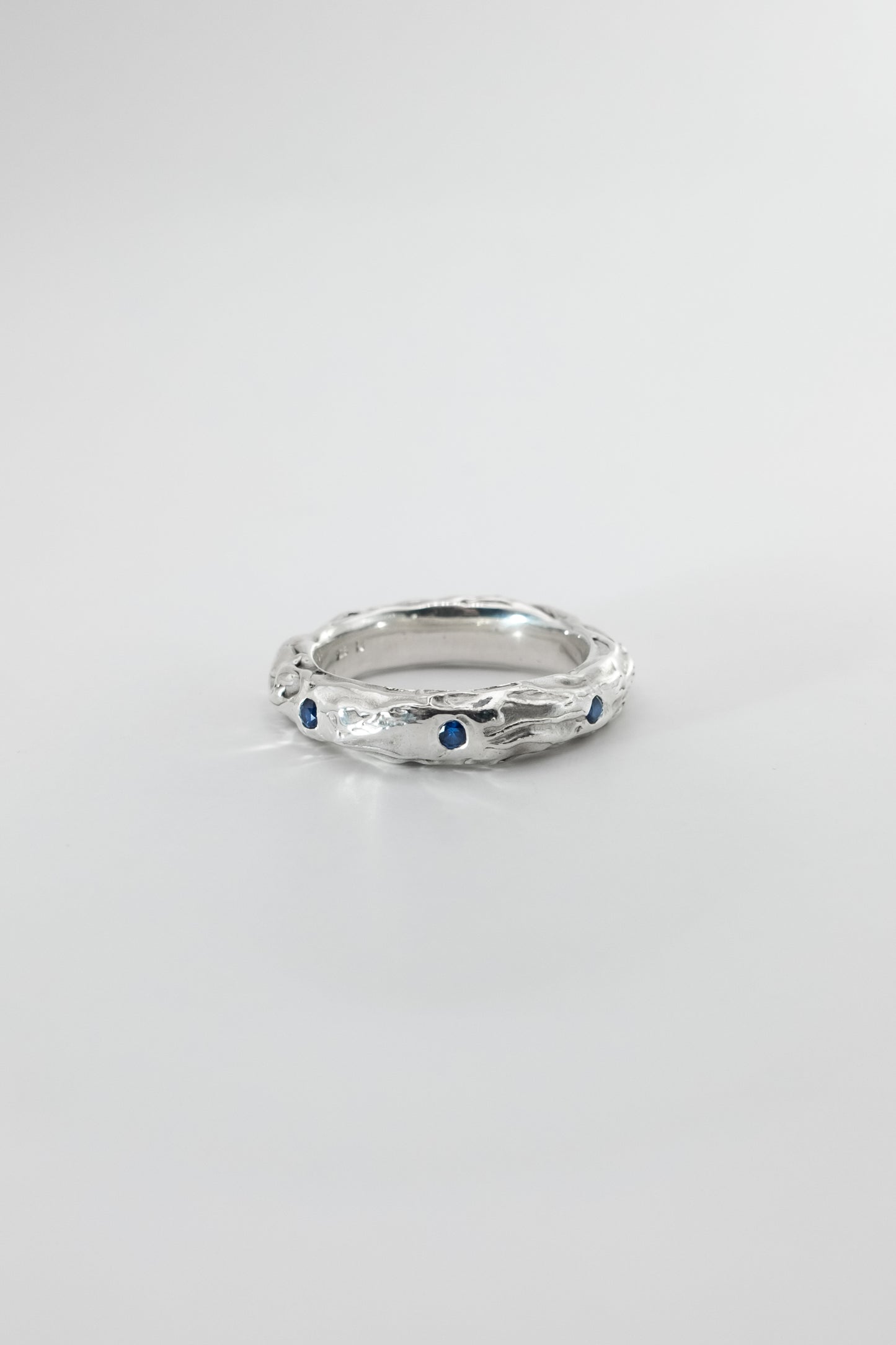 Silver ring with embedded blue sapphires on a light gray background