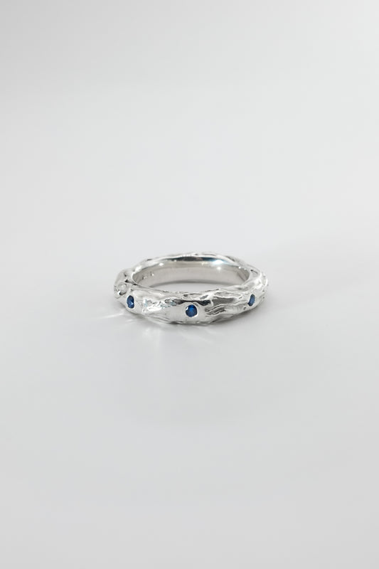 Silver ring with embedded blue sapphires on a light gray background