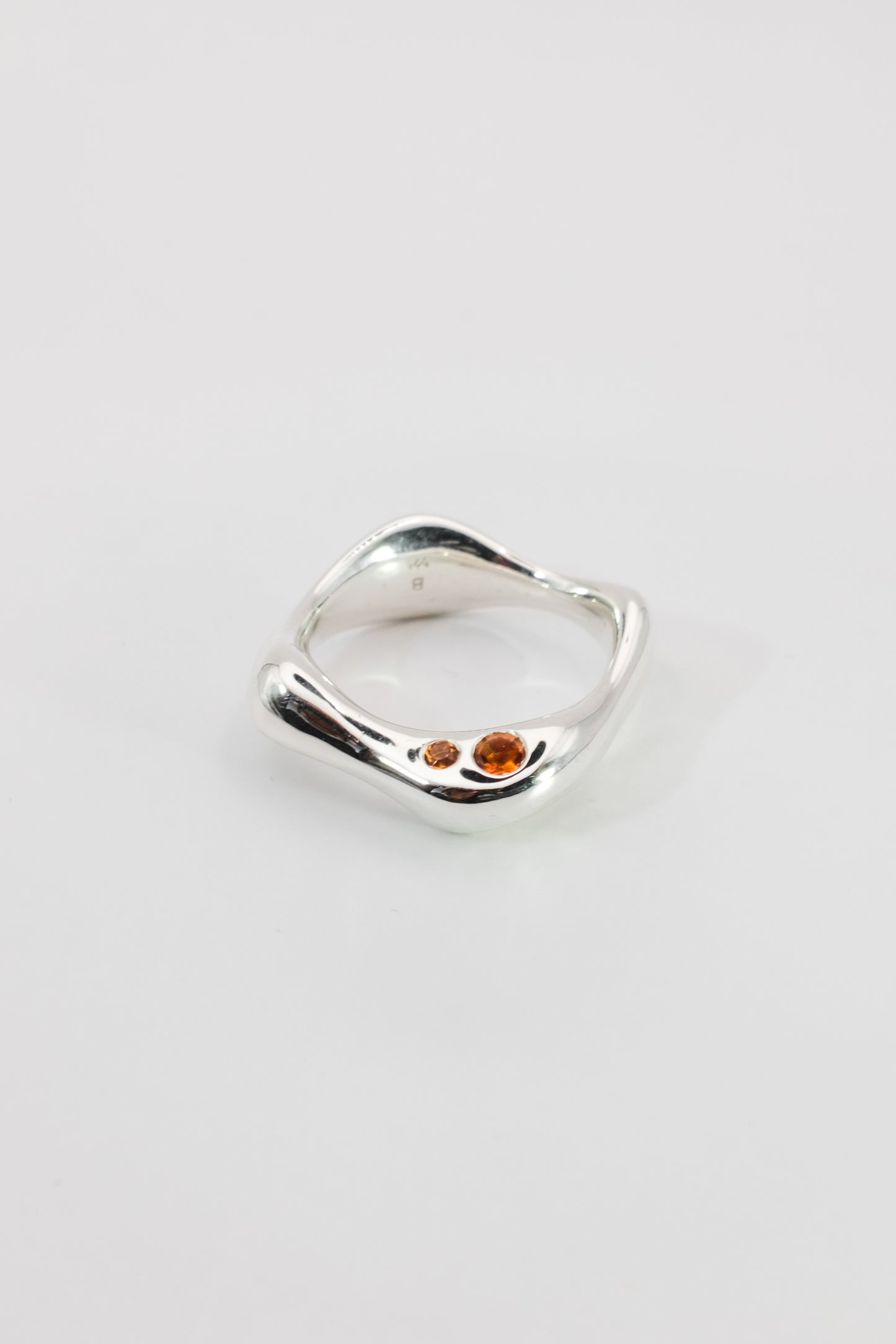 Smoothly shaped organic Silver ring with embedded Madeira Citrine gemstones on a light gray background