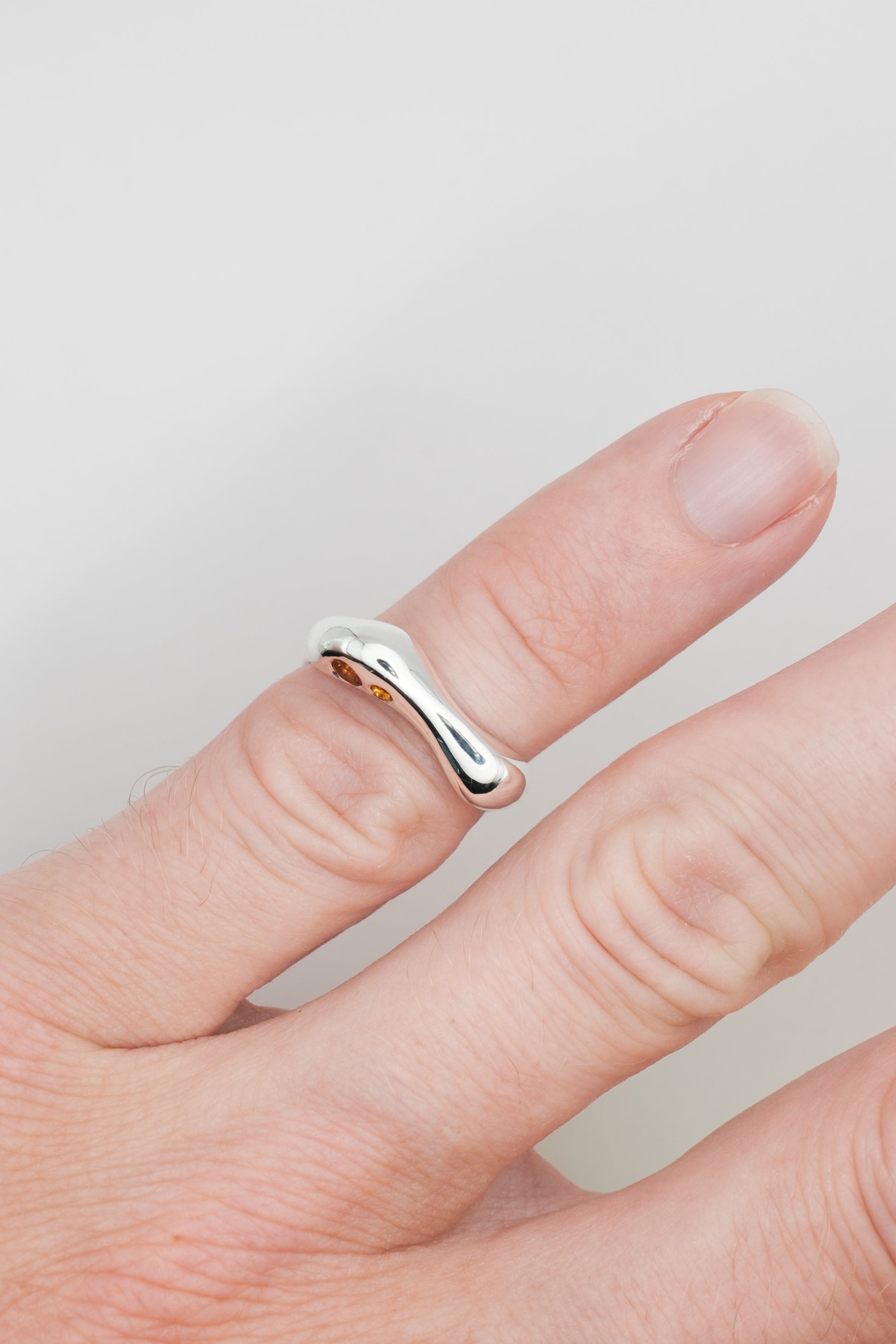 Silver ring on a finger against a plain background