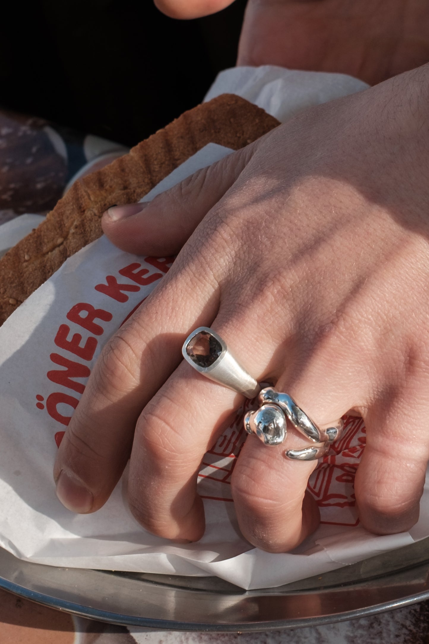 Close-up of a hand wearing two silver rings on a paper bag background