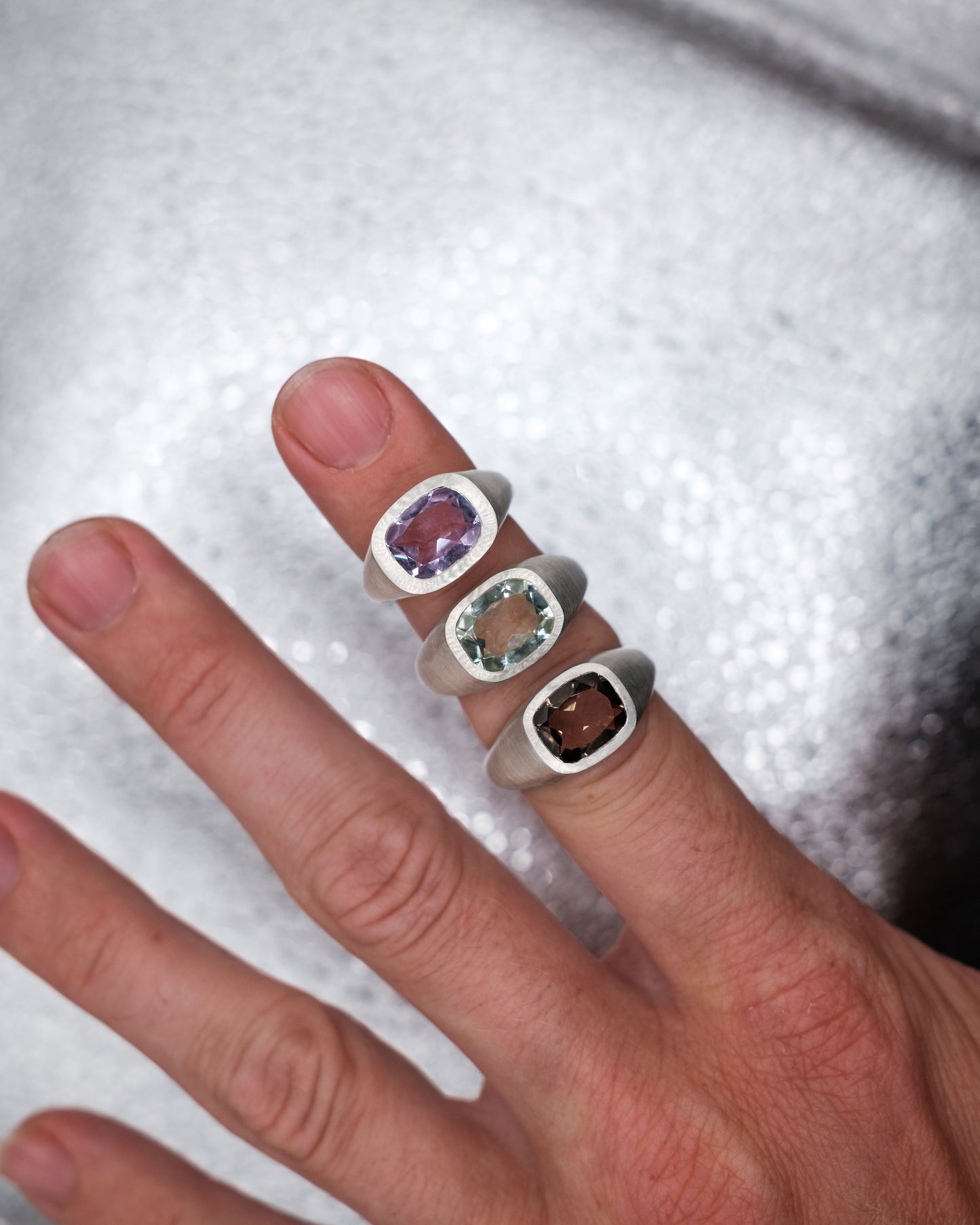 Hand wearing multiple silver rings with gemstones on a textured white background