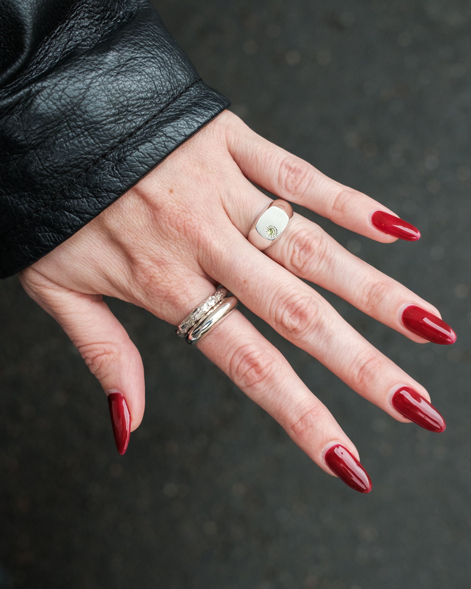 Hand with red nails wearing two rings on a dark background