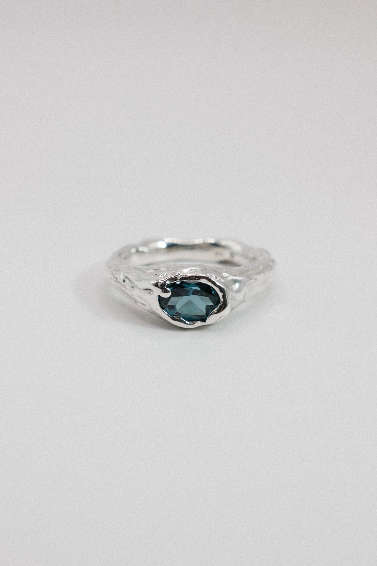 A silver ring with a textured, organic-shaped band and a central oval dark blue gemstone, shown on a plain light gray background.