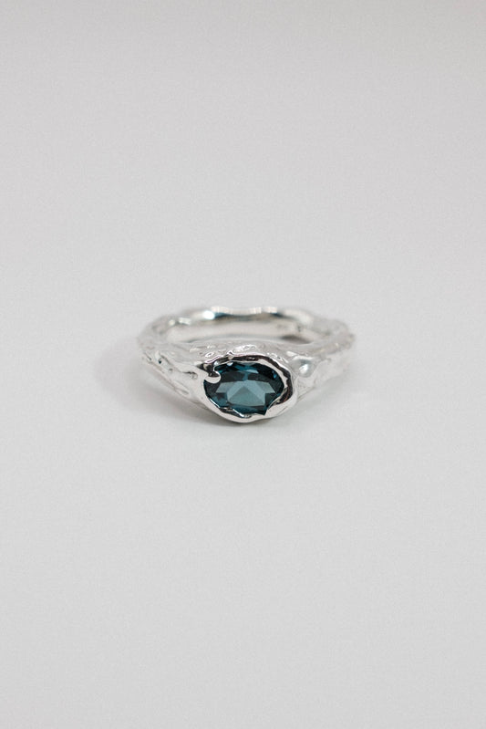 A silver ring with a textured, organic-shaped band and a central oval dark blue gemstone, shown on a plain light gray background.