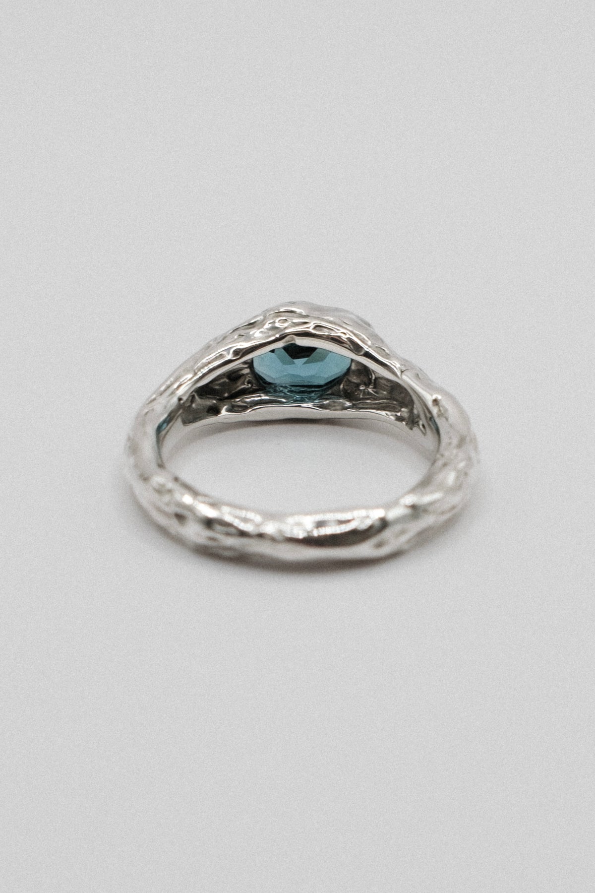 A textured sterling silver ring with a small oval light blue gemstone in the center, shown on a neutral light gray background.