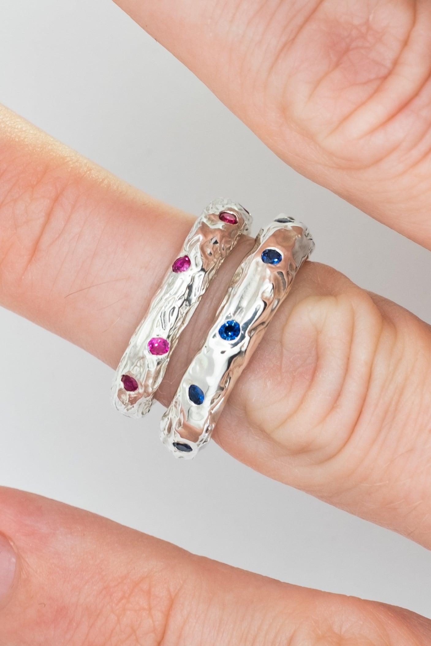 Silver rings with colorful gemstones on a finger against a neutral background