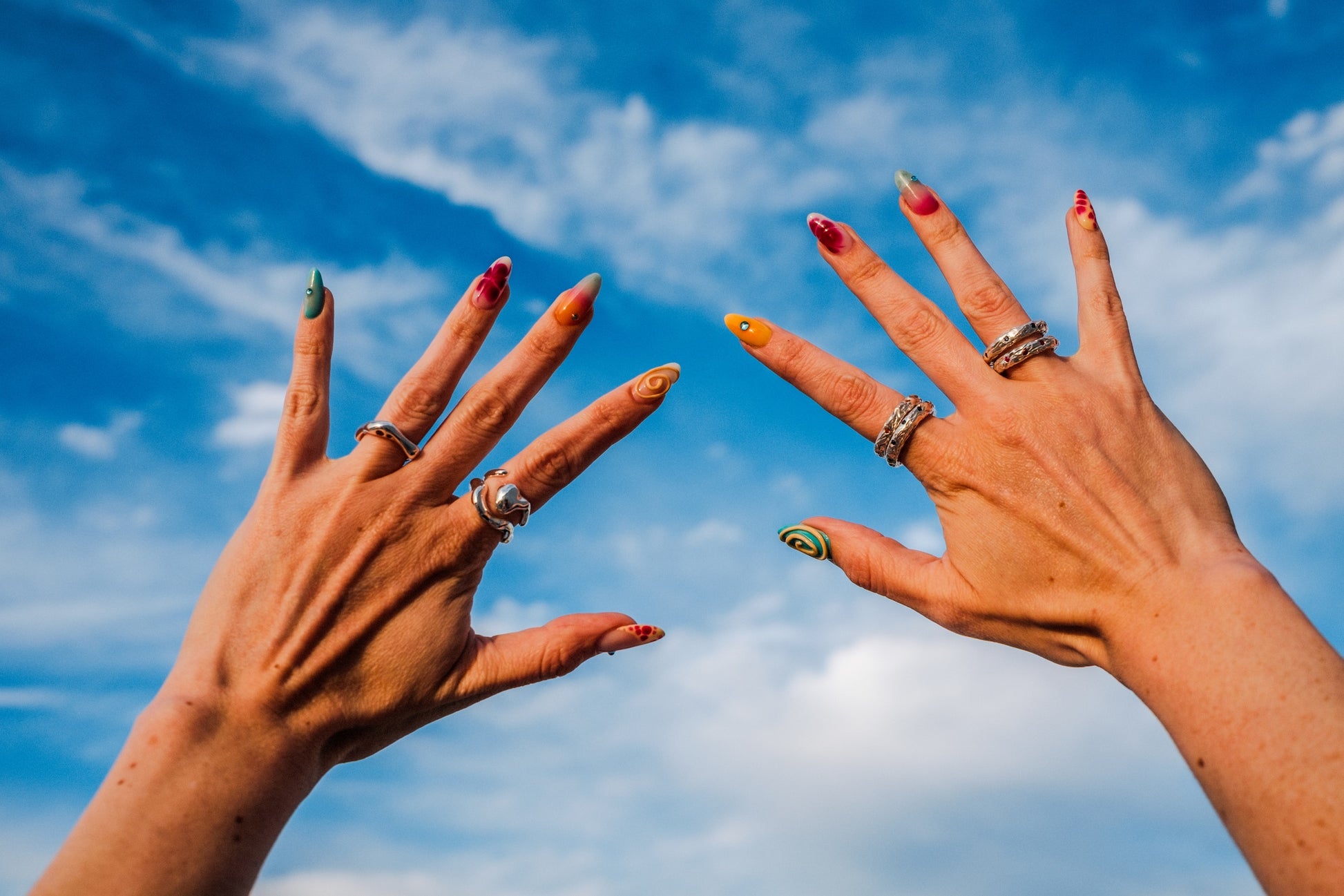 Two hands with painted nails and rings against a blue sky