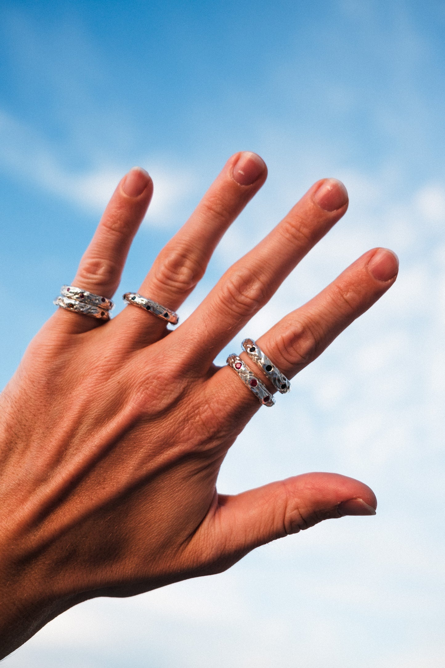 Hand wearing multiple rings with a blue sky background