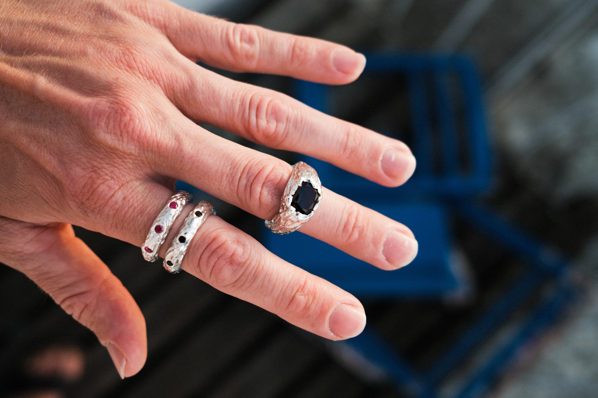 Hand wearing multiple bespoke rings with a blurred background