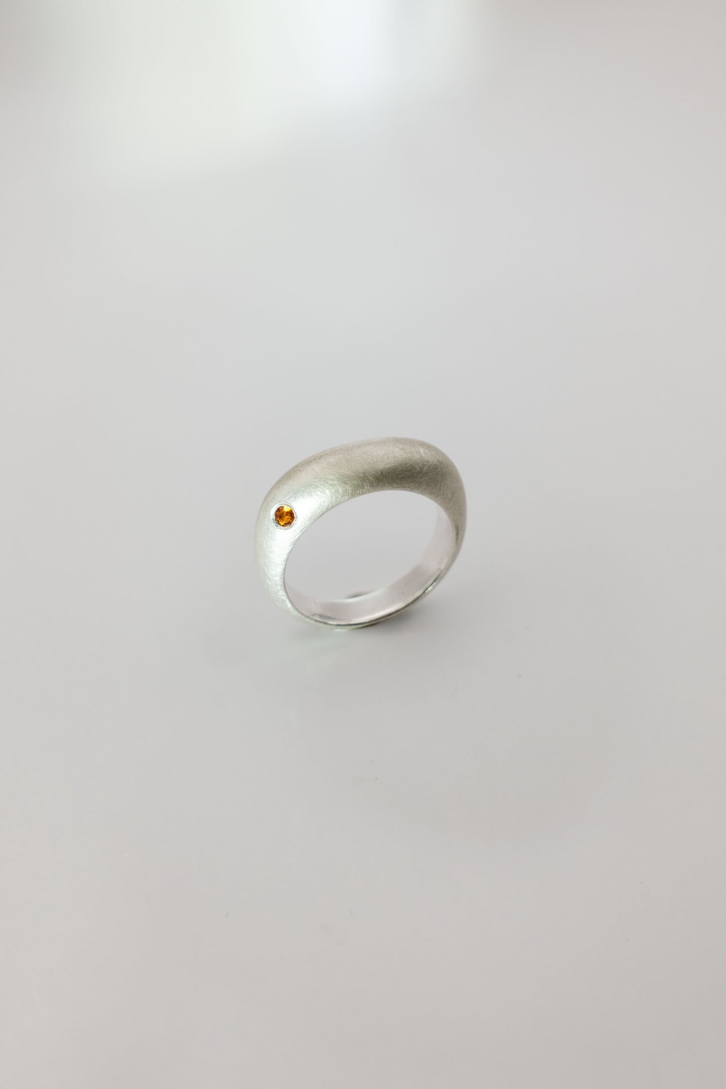 Silver ring with a small red gemstone on a light gray background