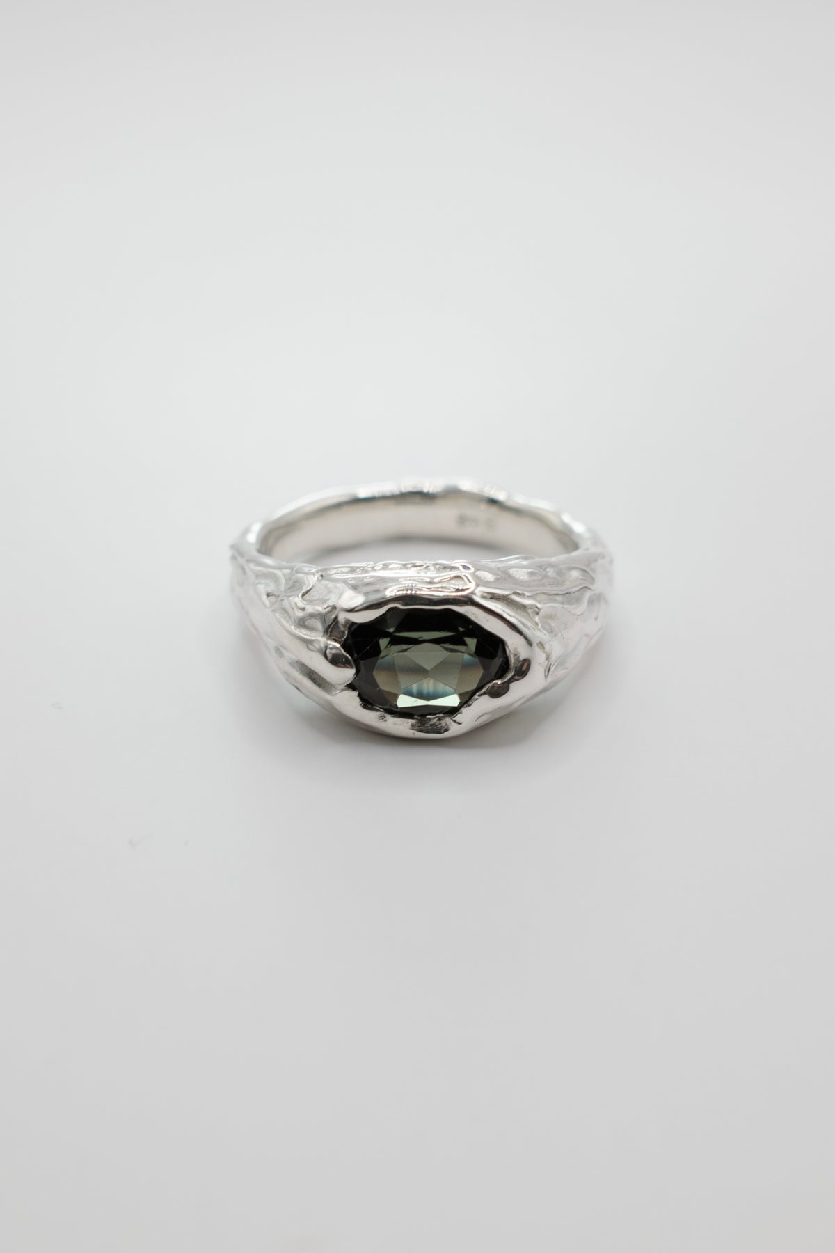A silver ring with a textured, hammered band and a central dark green faceted gemstone, shown on a plain light gray background.