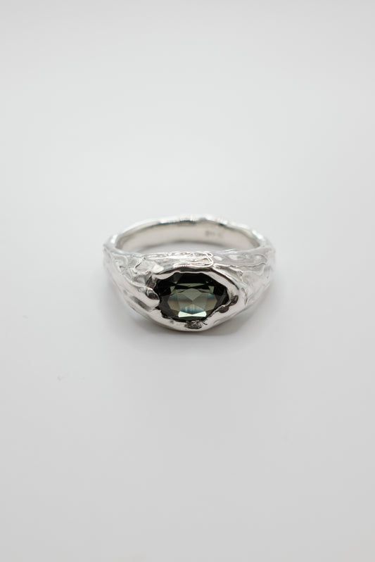 A silver ring with a textured, hammered band and a central dark green faceted gemstone, shown on a plain light gray background.