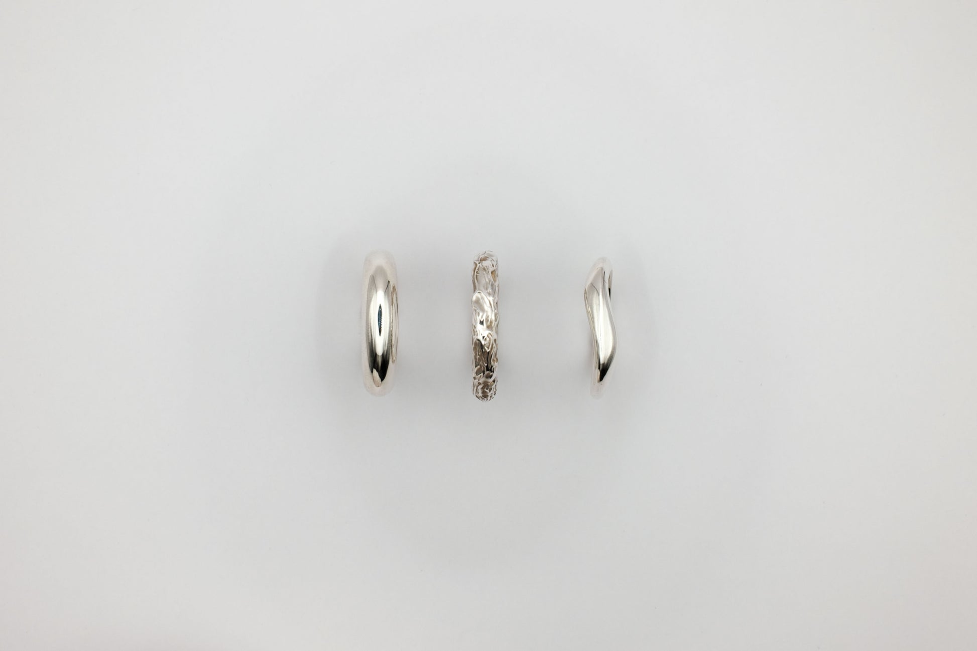 Three silver rings of different designs on a light gray background